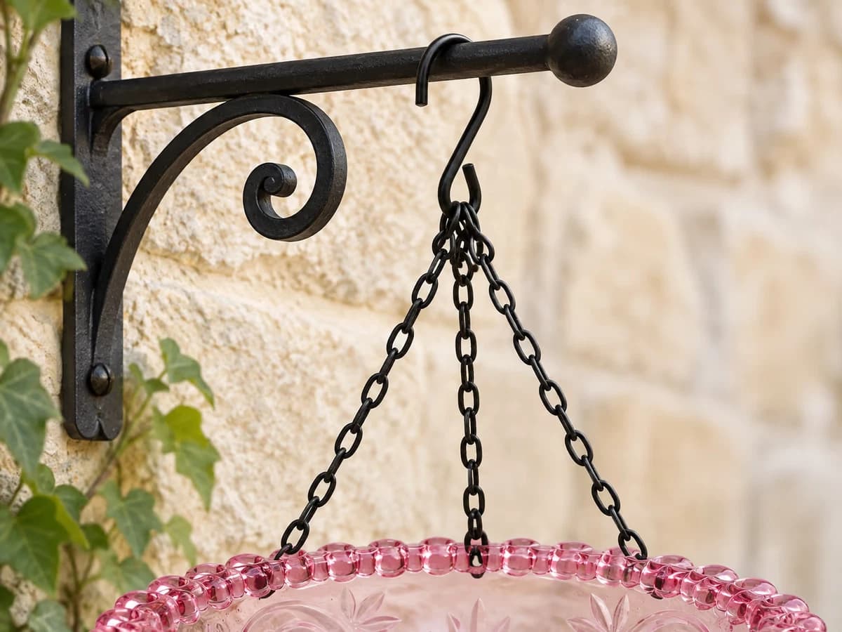 Détail d'un crochet ouvert passé sur le bras d'une potence de jardinière en fer forgé, avec la suspension raccourcie au plus près du support