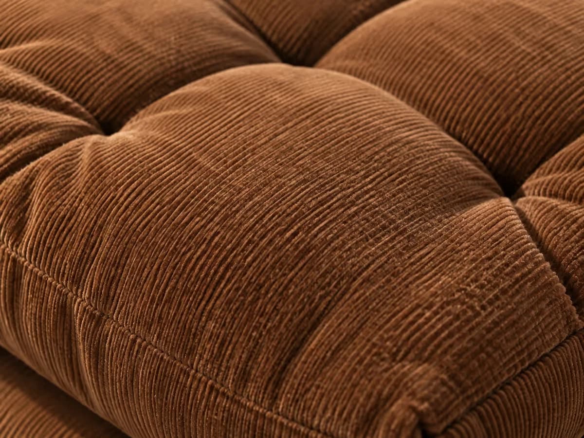 Gros plan en lumière rasante des côtes d'un coussin en velours côtelé marron, capitonnage piqué en carrés
