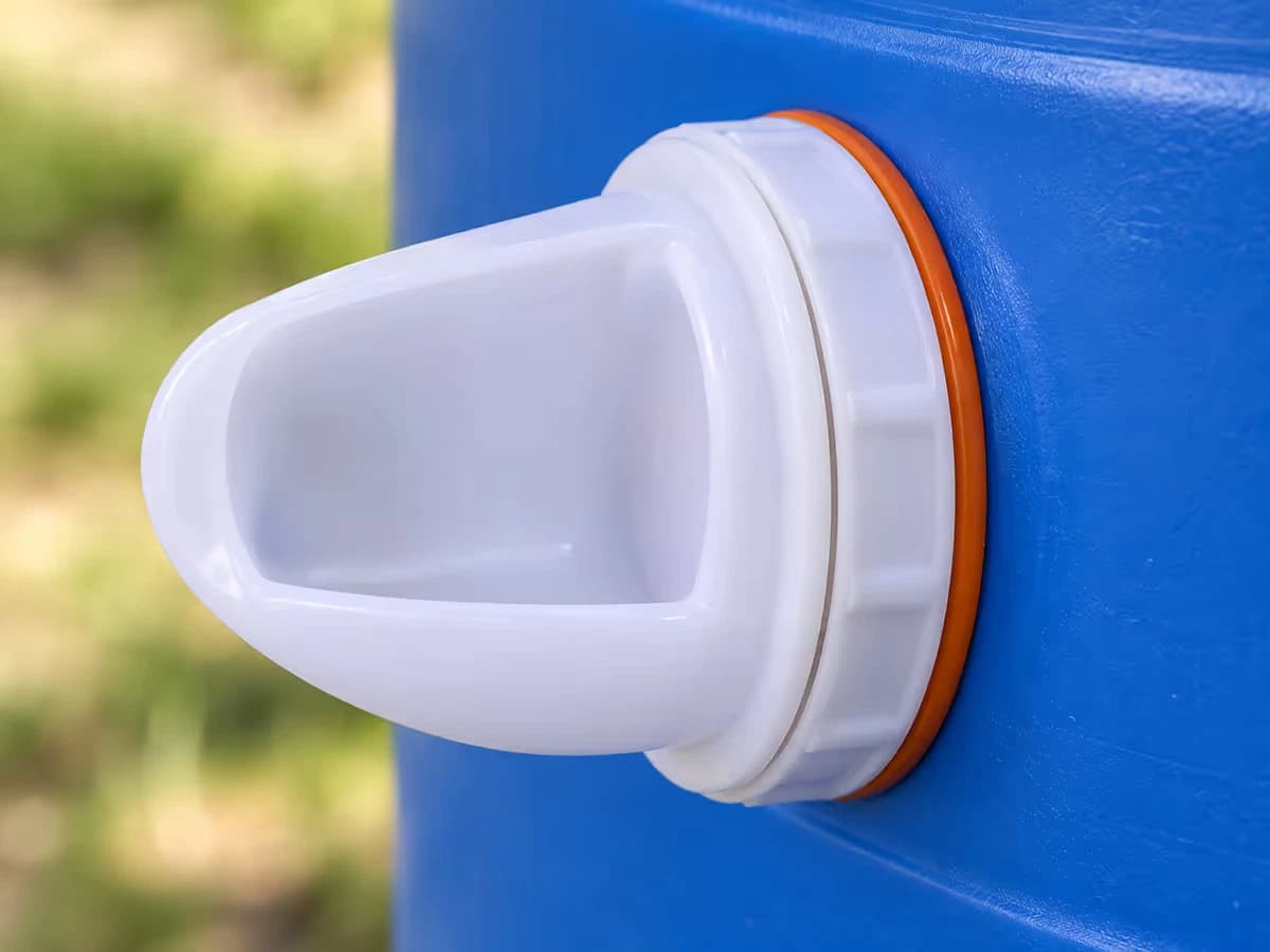 Gros plan d'un port blanc engagé dans la paroi percée d'un bidon, joint silicone orange logé entre le corps et la bague, paroi propre sans copeau