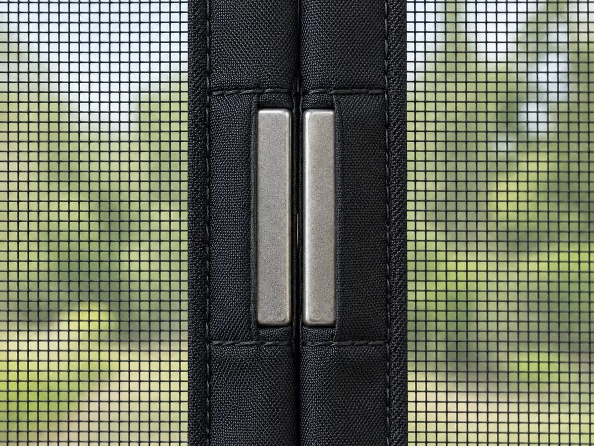 Détail de la rangée d'aimants rectangulaires cousus dans les bords des deux pans d'un rideau moustiquaire noir, couture fermée sur toute la hauteur
