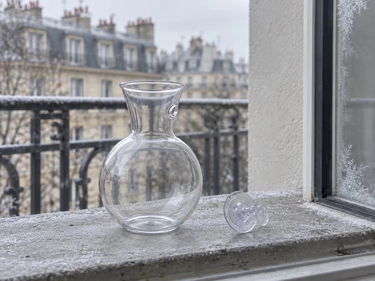 Vase mural transparent vide décroché de la vitre, posé sur un rebord de balcon avec des traces de givre sur le carreau