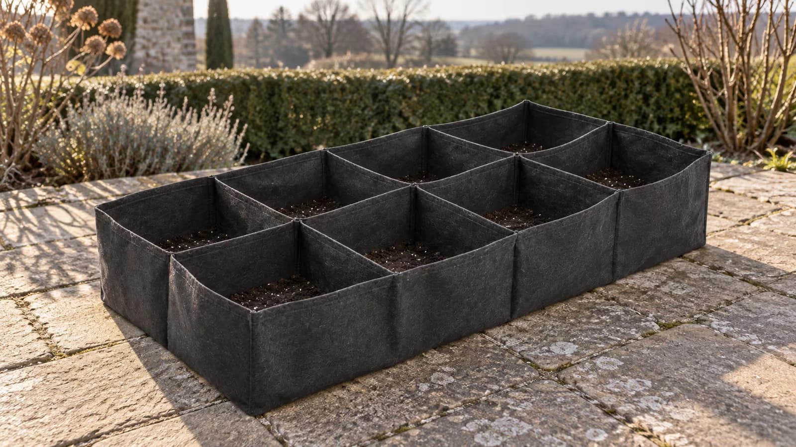 Bac potager surélevé en tissu feutré déplié et vide sur une terrasse au soleil bas de mars, cellules béantes