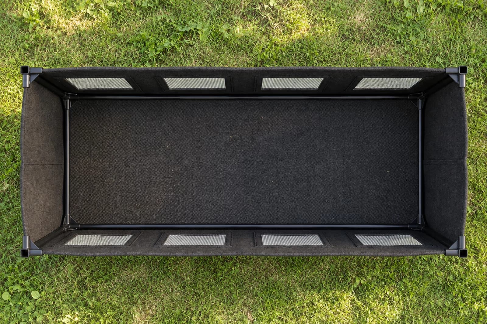 Vue top-down 80 degres du bac potager en tissu noir deplie et vide, structure metal et 8 fenetres d'aeration alignees visibles