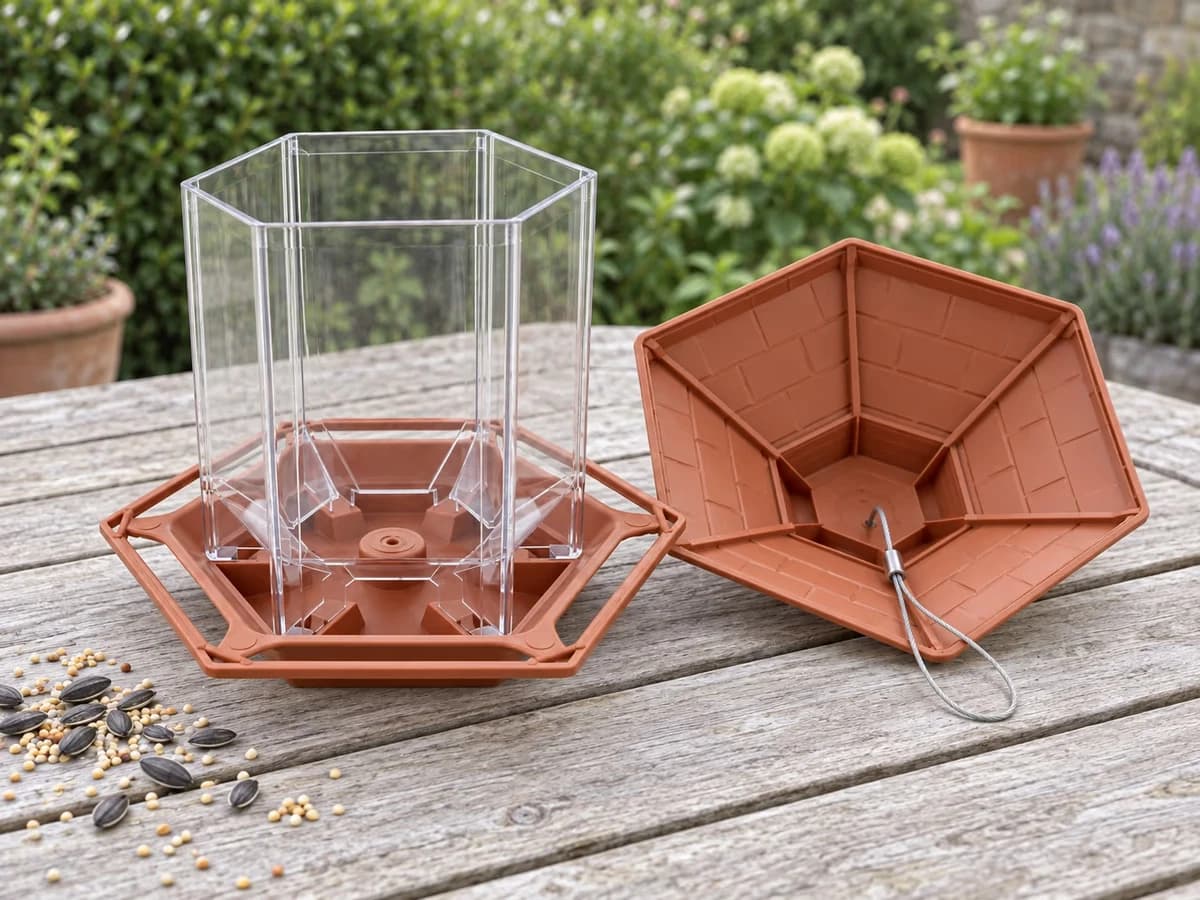 Mangeoire à silo hexagonale ouverte sur une table de jardin, toit posé à côté et sorties de graines visibles