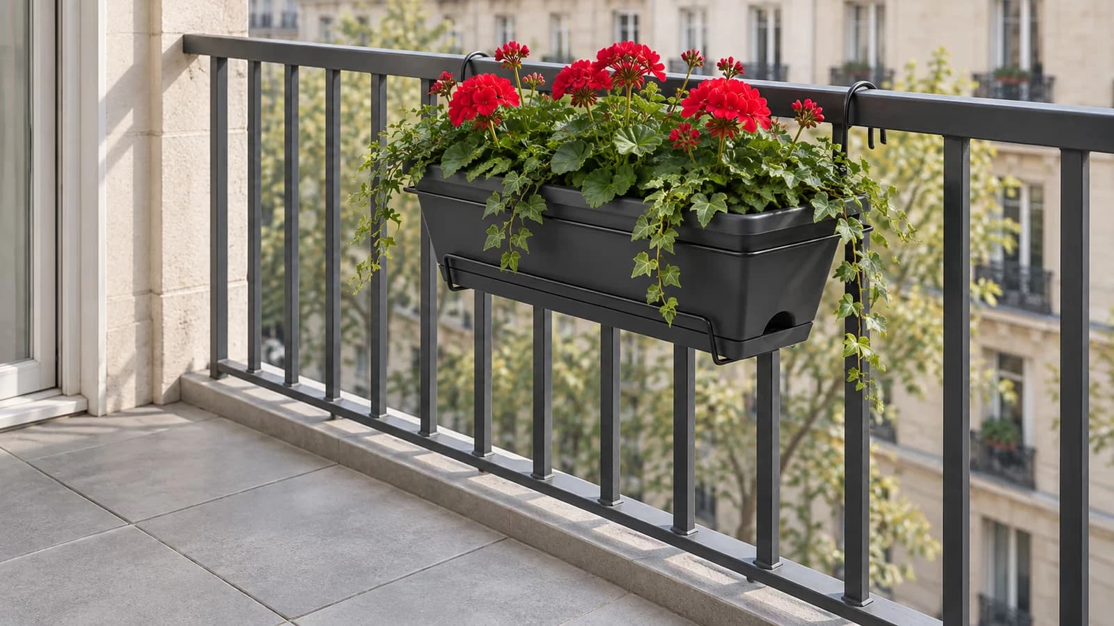 Jardinière rectangulaire gris foncé dans son support filaire à deux crochets, posée sur le dessus d'un garde-corps métallique vue depuis l'intérieur du balcon