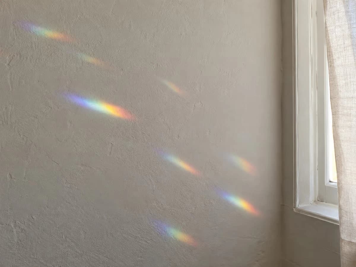 Taches de couleur projetées sur un mur clair par un attrape-soleil suspendu devant un carreau de fenêtre en plein soleil