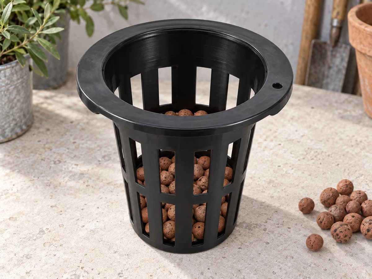 Billes d'argile versées au fond d'un panier en maille noire posé sur un plan de travail clair, couche régulière visible depuis le dessus