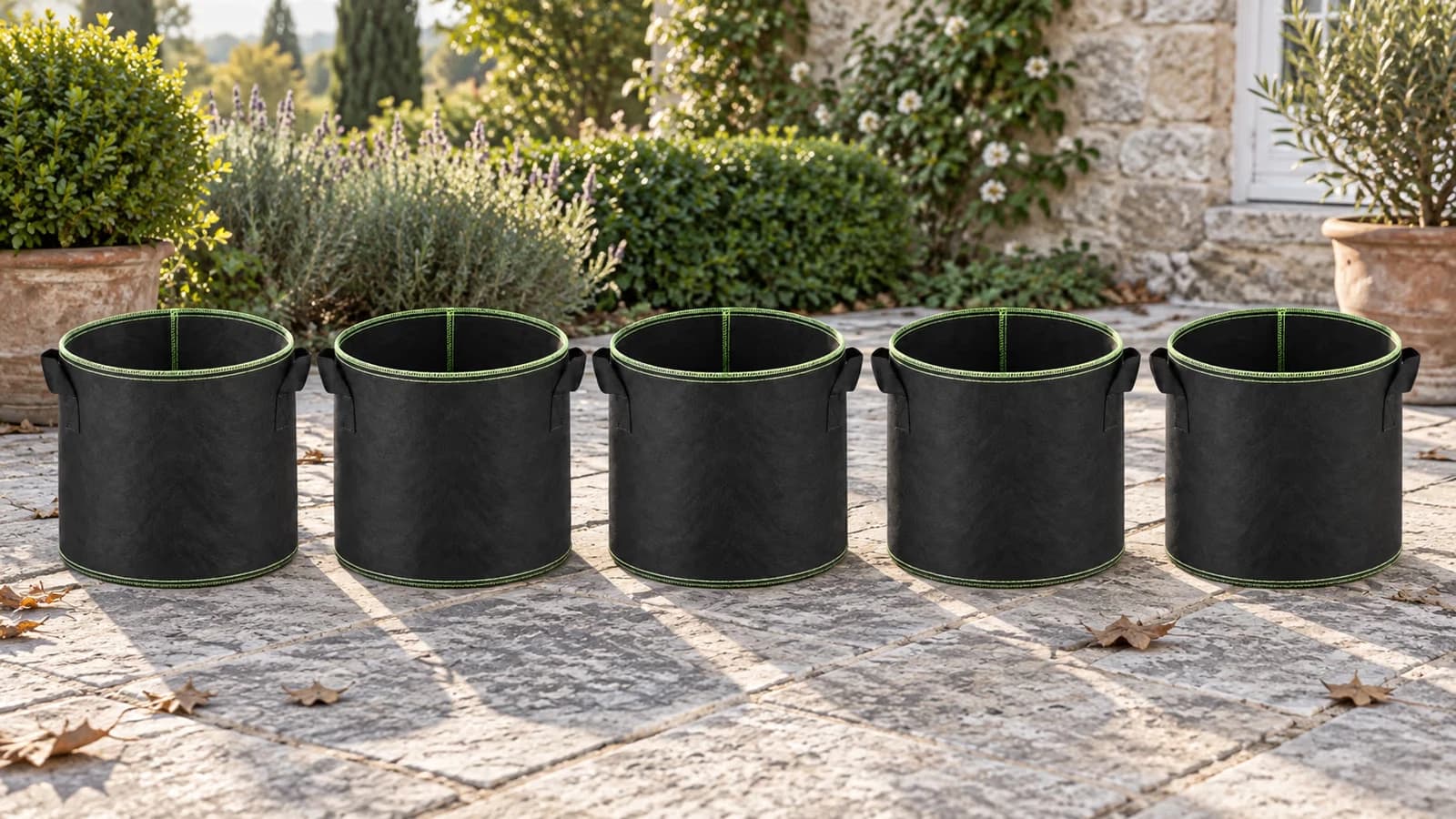 Cinq sacs de plantation noirs alignés vides sur une terrasse claire, poignées latérales visibles, lumière du matin