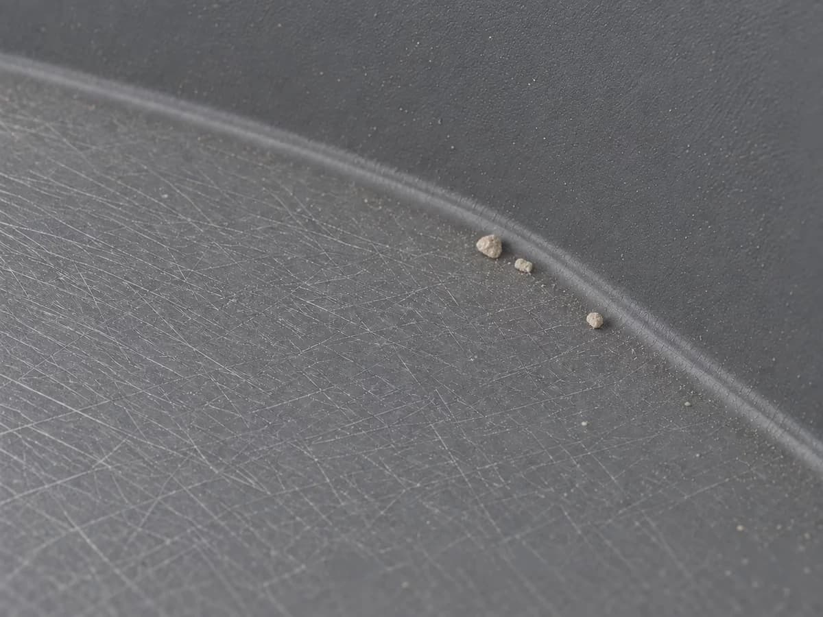 Fond d'une cuve de bac de propreté en plastique gris, vu de près et en lumière rasante, réseau de fines rayures croisées dans la matière