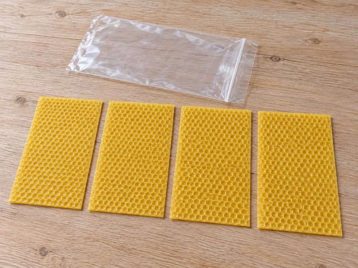 Quatre feuilles de cire gaufrée posées côte à côte sur une table claire, un sachet transparent ouvert à côté