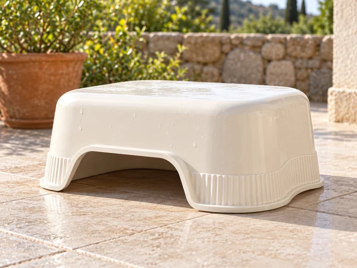 Bac de propreté en plastique posé à l'envers sur une terrasse carrelée, lèvre avant visible, lumière du matin et ombre courte