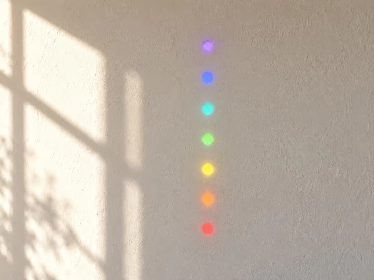 Sept taches rondes et distinctes de couleurs différentes alignées sur un mur blanc, projetées par une suspension proche du mur