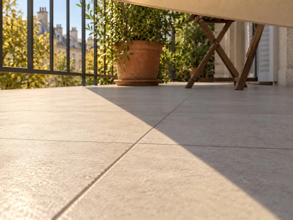 Ombre d'une voile triangulaire beige sur un carrelage de balcon, ligne de séparation entre zone éclairée et zone ombragée