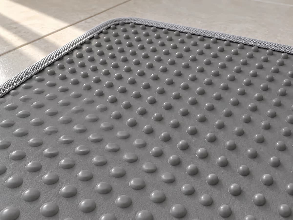 Gros plan sur la face inférieure d'un tapis de litière gris retourné, picots couchés dans une zone et dressés autour