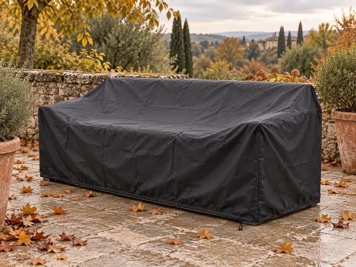 Housse noire posée et cordon serré sur un salon de jardin, sur une terrasse jonchée de feuilles mortes à l'automne