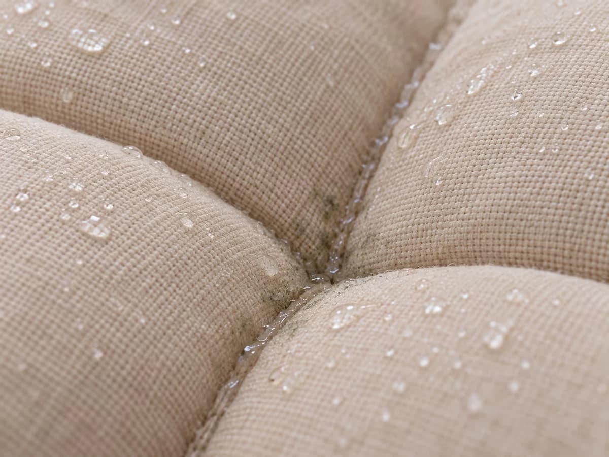 Gros plan sur une ligne de couture piquée d'un coussin d'assise beige, auréole gris-vert naissante le long du fil mouillé
