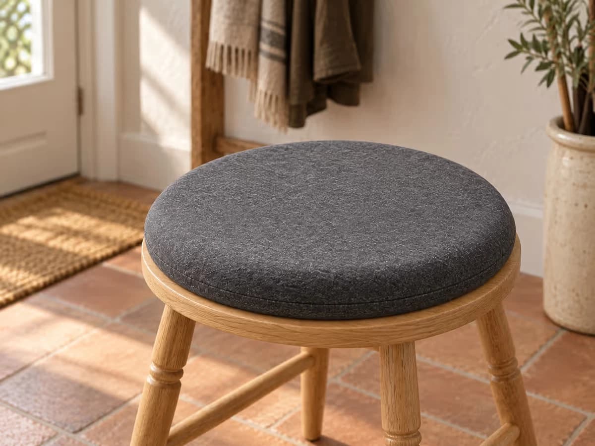 Galette de coussin ronde en tissu gris foncé posée au centre d'un tabouret d'entrée en bois, bord du coussin aligné avec le chant