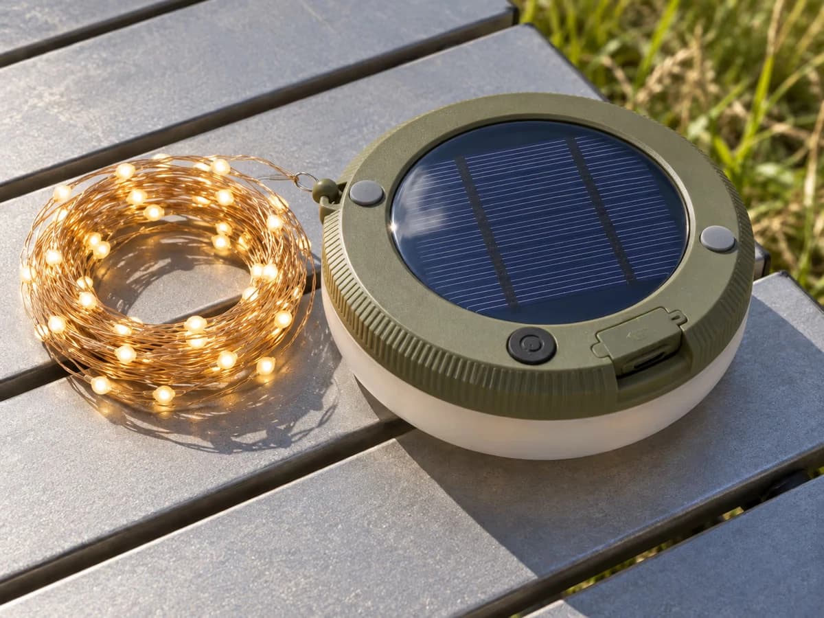 Boîtier de lampe solaire posé à plat sur une table de camping, panneau bleu en damier tourné vers le ciel, en plein soleil