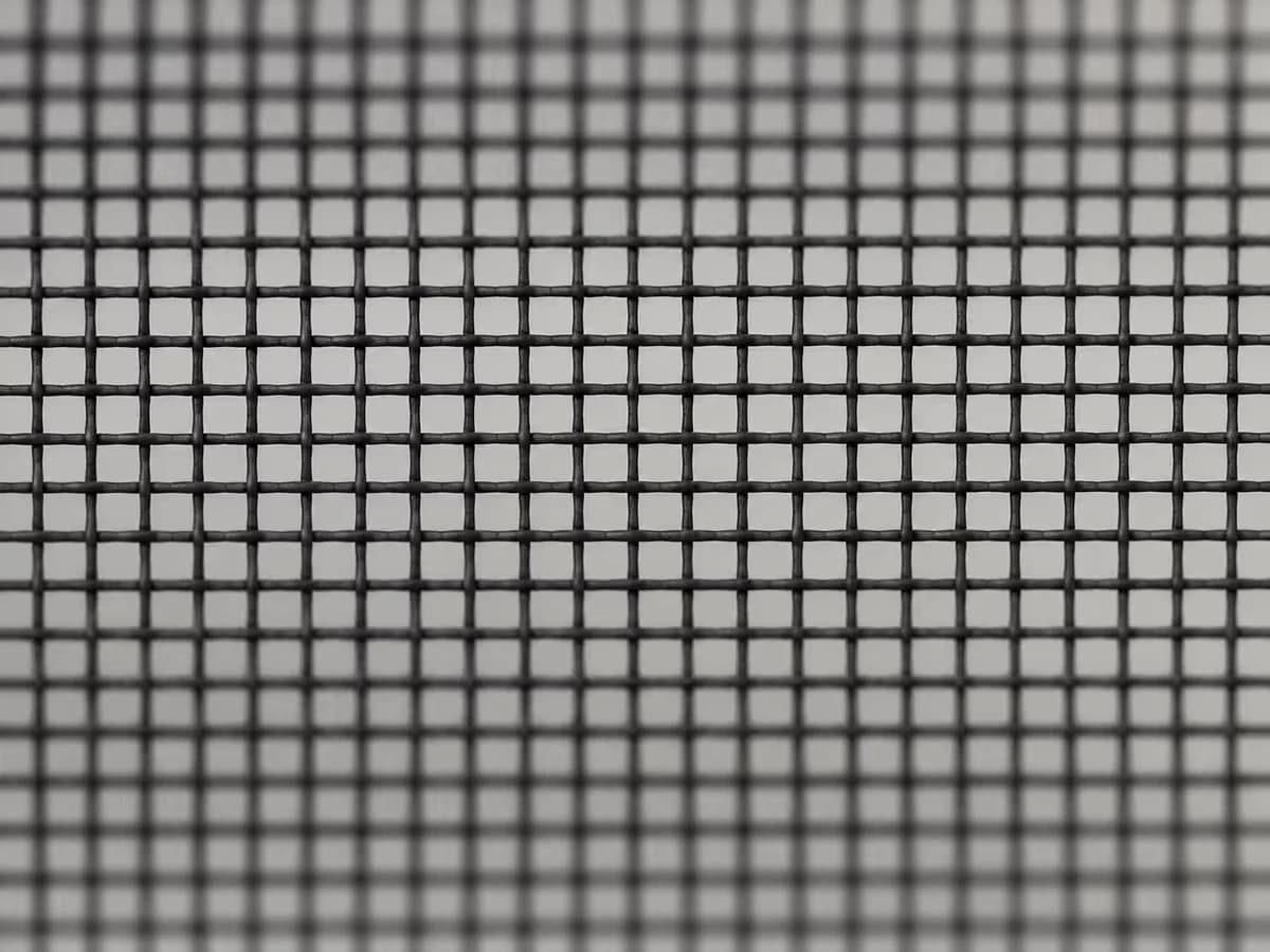Gros plan sur une maille de tulle moustiquaire noire, trame régulière éclairée en lumière rasante