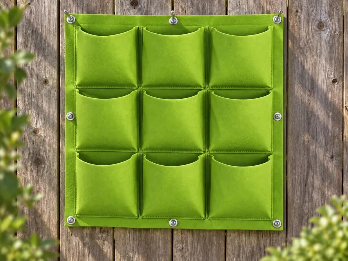 Huit vis à œil métalliques engagées dans les œillets d'un panneau de feutre vert clair tendu à plat sur un mur de clôture en bois