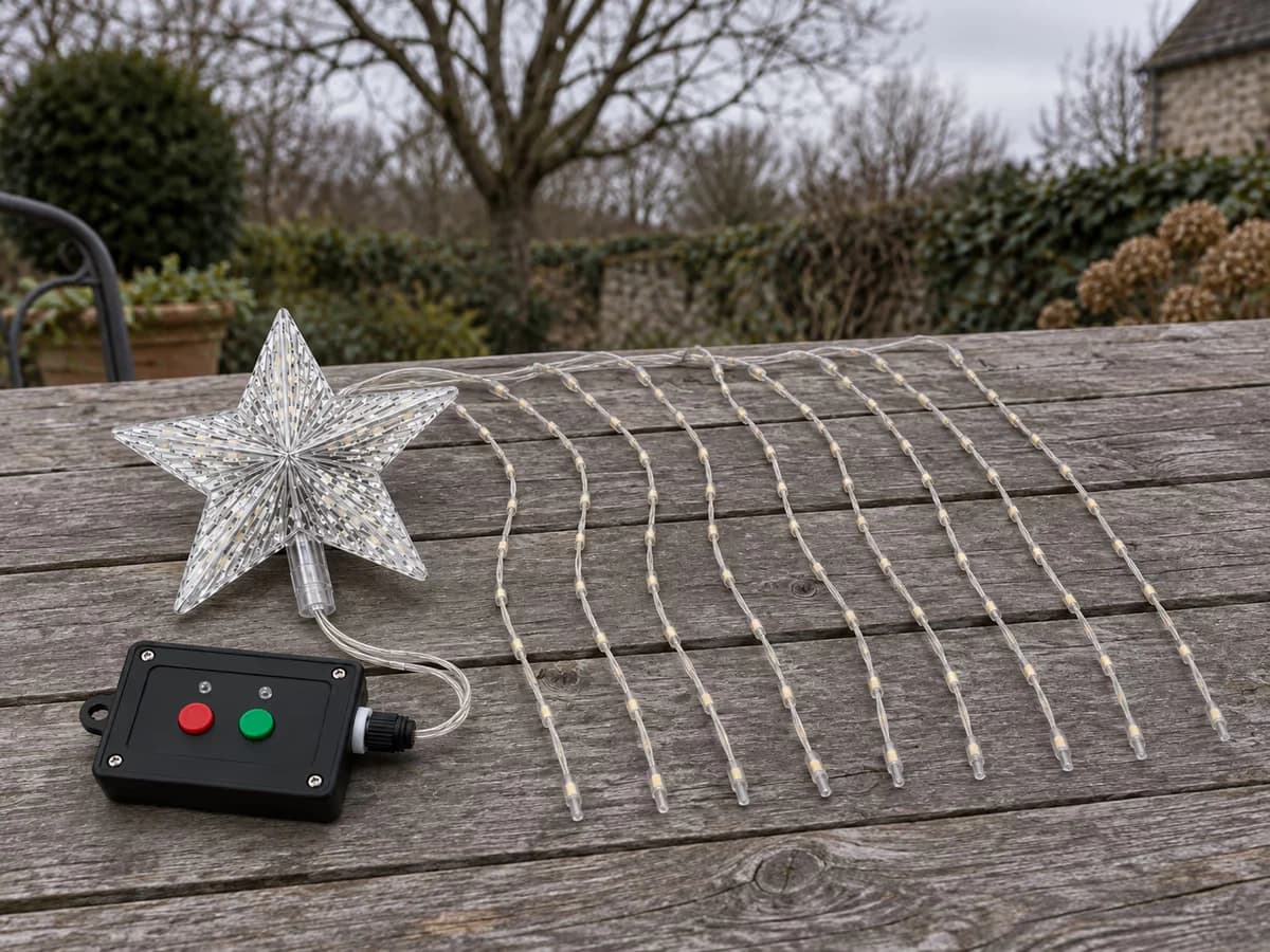 Étoile solaire déposée sur une table de jardin en fin d'hiver, neuf cascades déroulées à plat à côté du boîtier noir, branche nue en arrière-plan