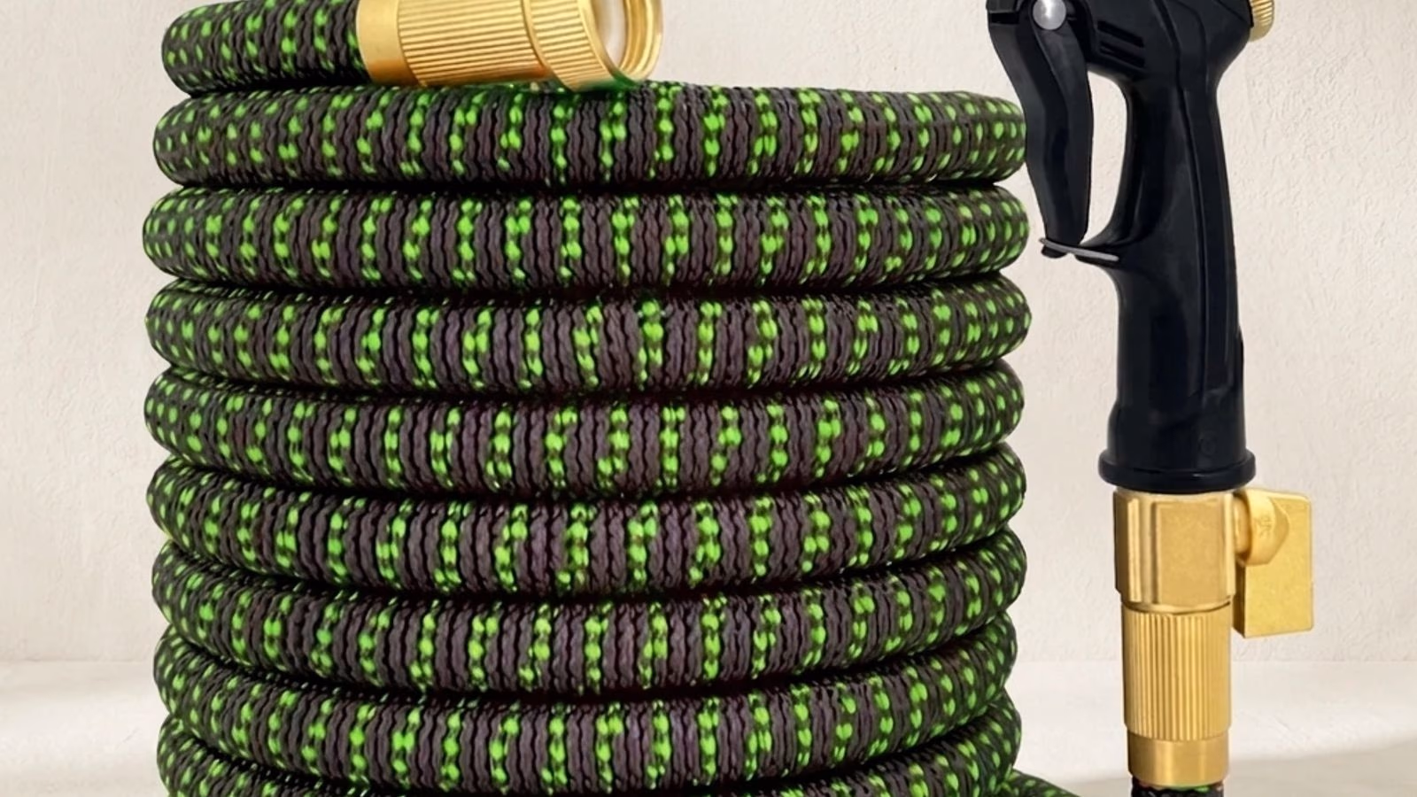 Tuyau d'arrosage extensible 30 m enroulé avec raccords laiton dorés et pistolet 8 modes sur fond studio clair