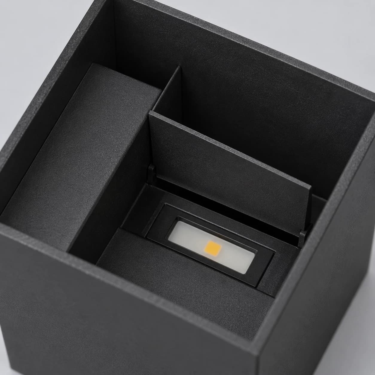 Le volet ouvert du cube noir découvre la barrette LED et sa pastille dorée au fond de la cavité