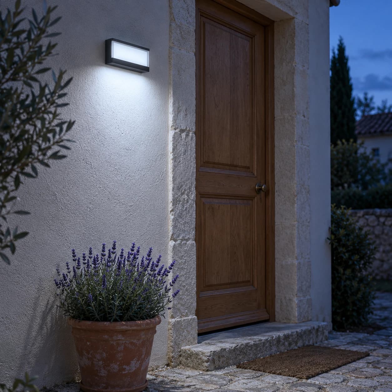 L'applique allumée sur le mur d'une entrée en pierre, au-dessus d'une potée de lavande