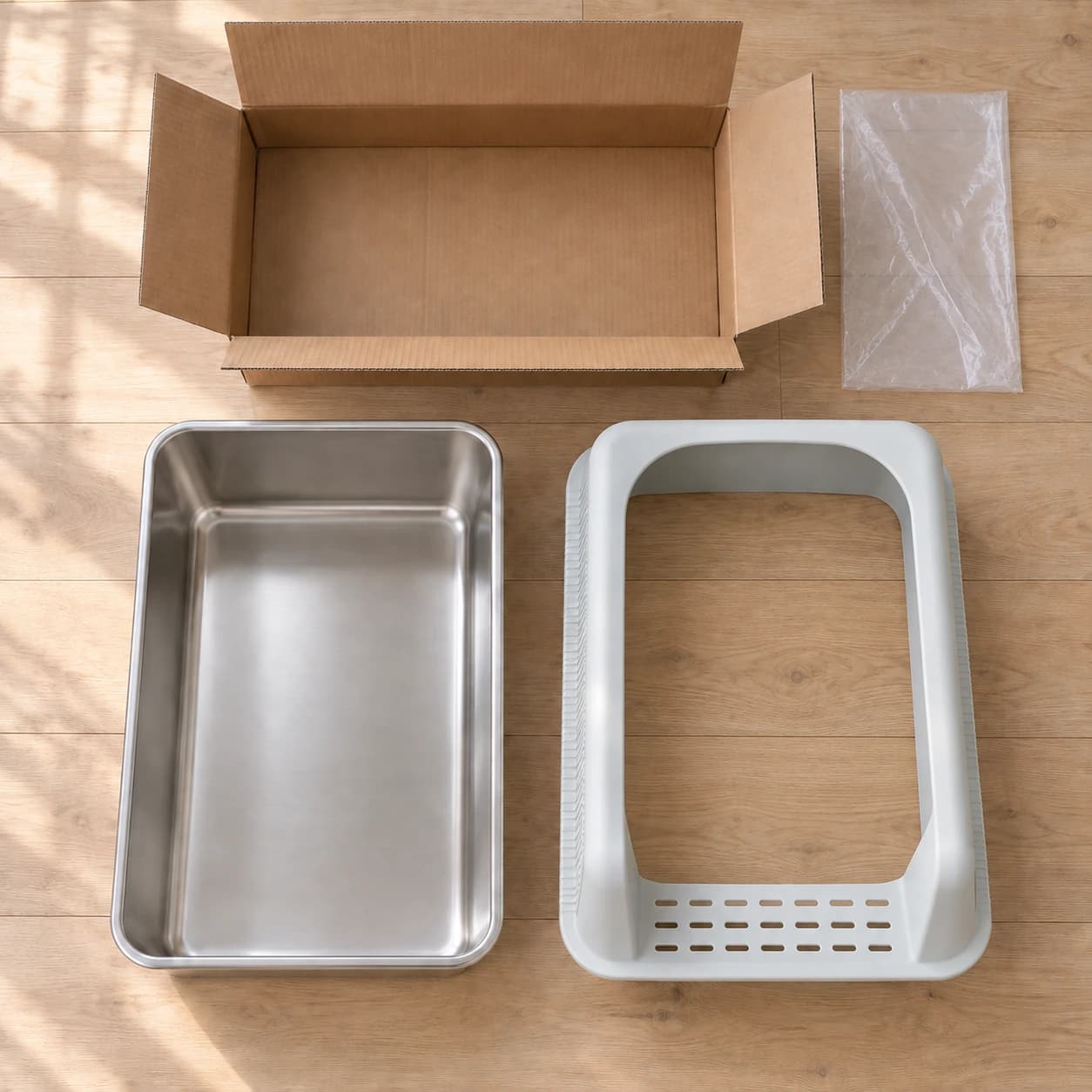 Contenu du colis posé à plat : cuve inox, rebord gris clair et carton d'emballage