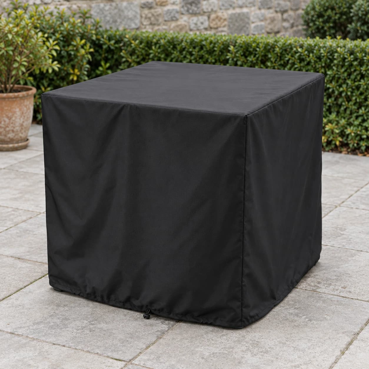 Housse noire enveloppant une table de jardin carrée sur une terrasse en dalles béton claires