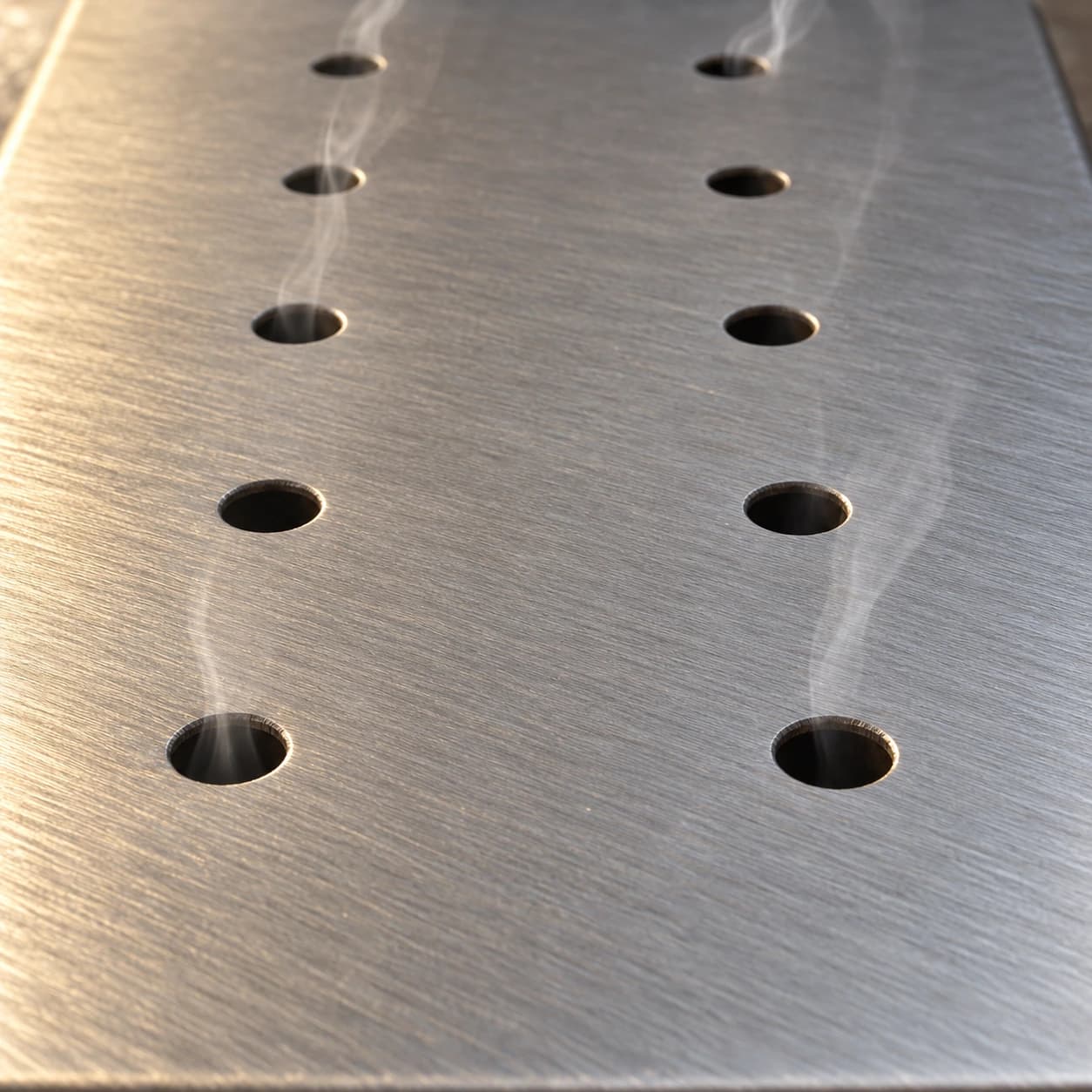 Détail du couvercle en inox brossé : deux rangées de six trous, filets de fumée