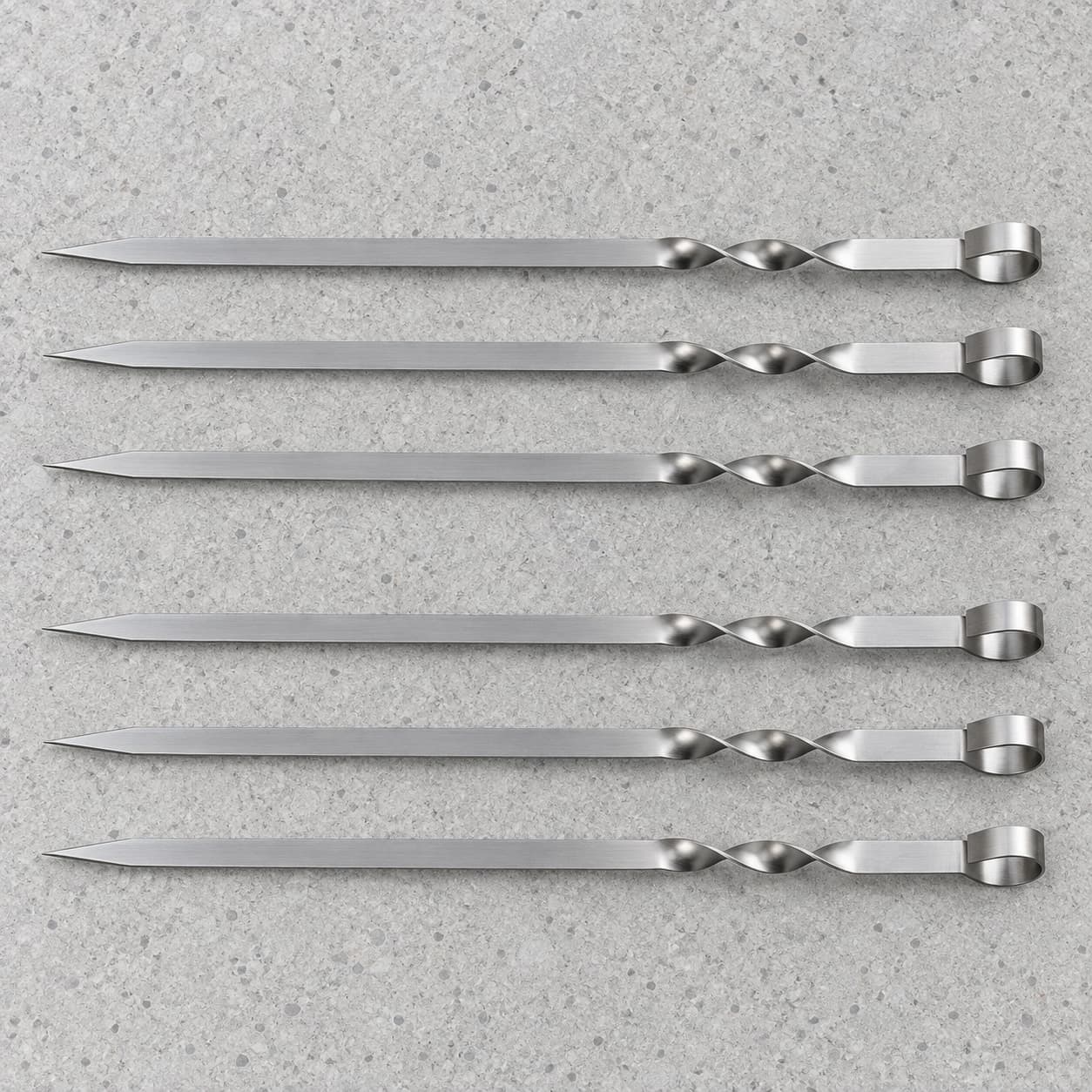Les six brochettes inox de 50 cm posées à plat en deux rangées de trois sur une pierre claire