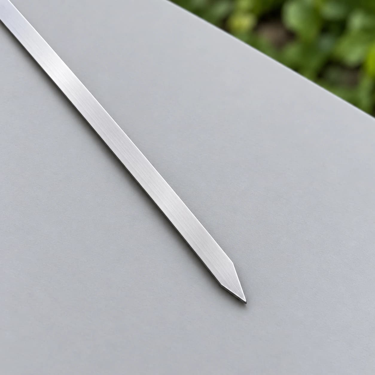 Pointe biseautée d'une pique plate en inox satiné posée sur une surface mate grise