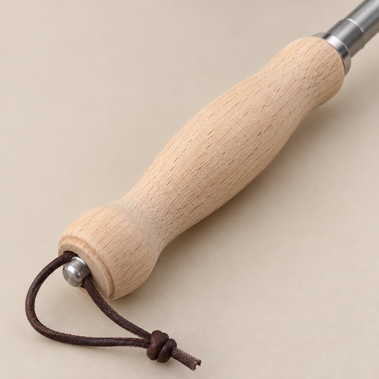 Gros plan du manche tourné en bois clair, avec sa dragonne de cuir nouée et le collier en inox