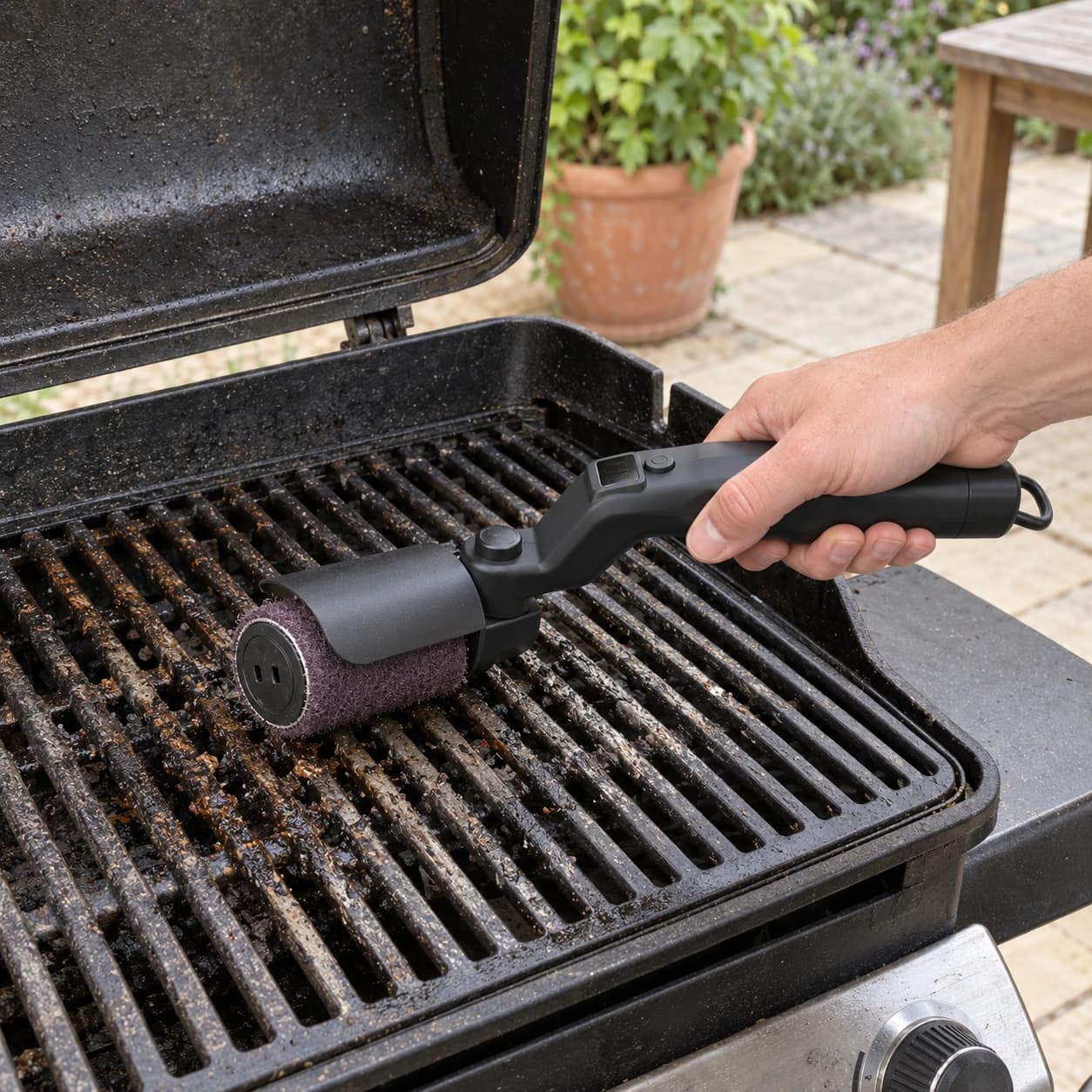 Brosse électrique tenue en main au-dessus d'une grille de barbecue, tampon violet au contact des barreaux