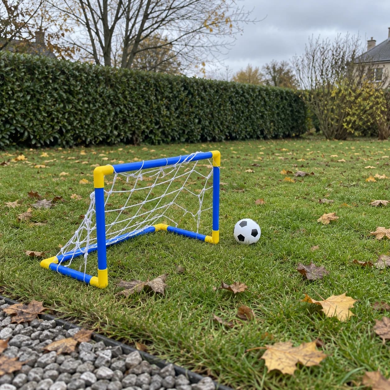 Le but miniature et son ballon sur la pelouse d'un jardin, feuilles d'automne et haie taillée
