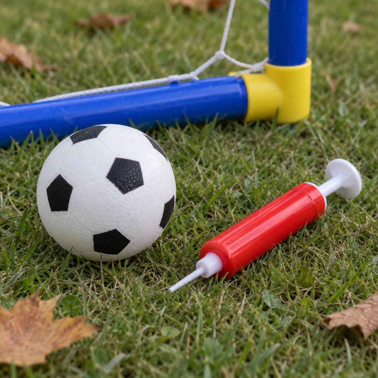 Le ballon à pentagones noirs et la pompe à air rouge posés sur l'herbe, coin du cadre derrière
