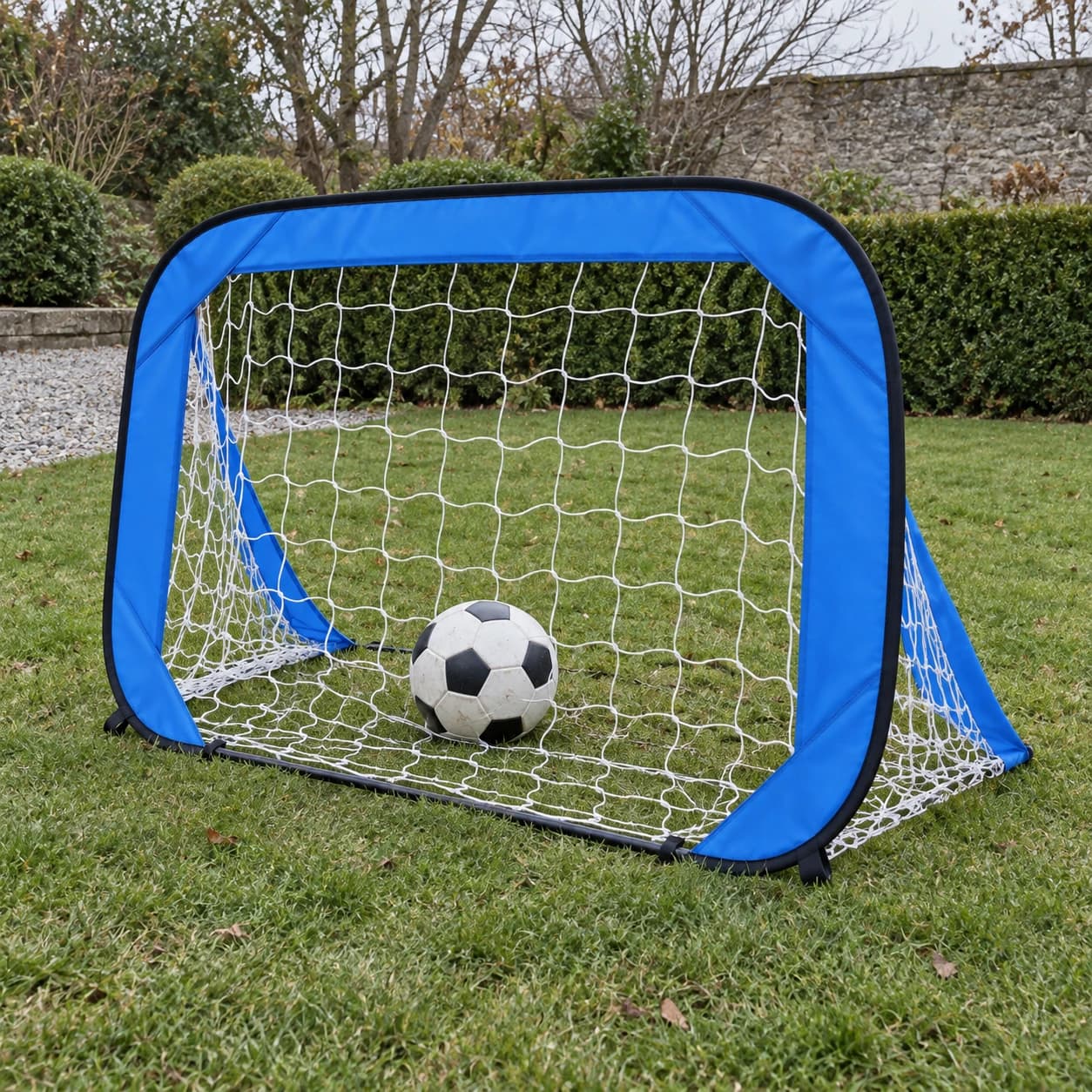 But de football pop-up enfant monté sur une pelouse de jardin, filet blanc et ballon posé dans la cage