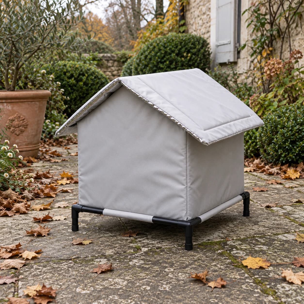 Cabane pour chat sur pied vue de l'arriere sur une terrasse en pierre, dans un jardin d'automne