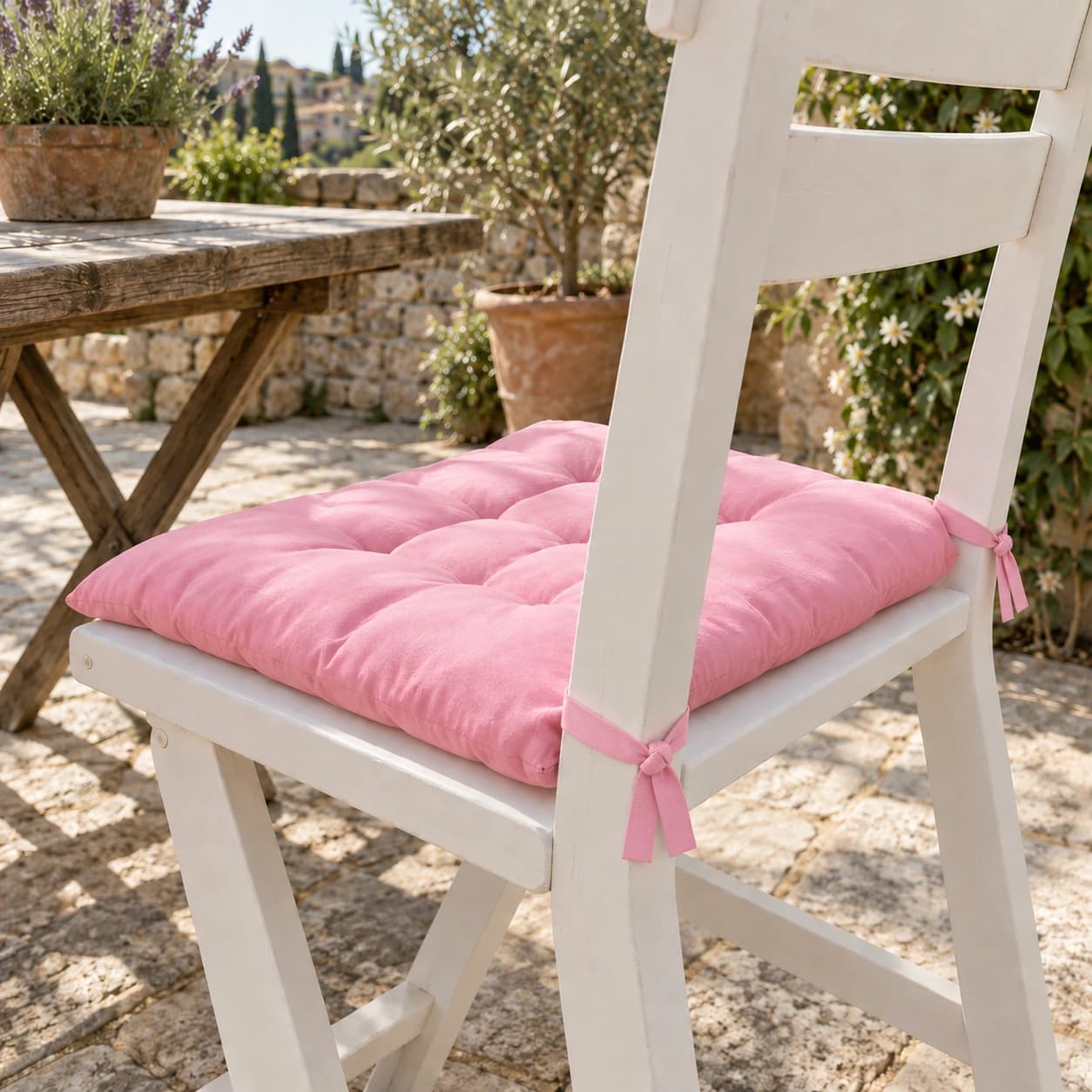 Coussin d'assise rose capitonné sur une chaise de jardin blanche, terrasse en pierre provençale