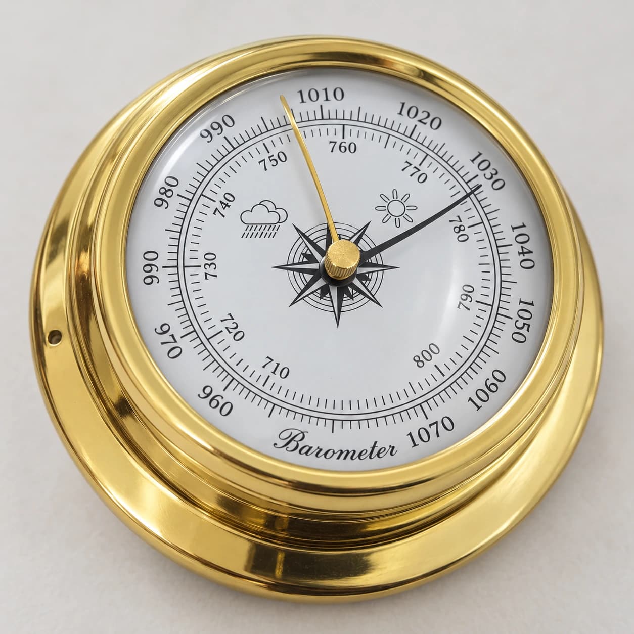 Gros plan du baromètre doré, graduation de 950 à 1070 hPa, aiguille noire, aiguille de référence dorée et cabochon moleté