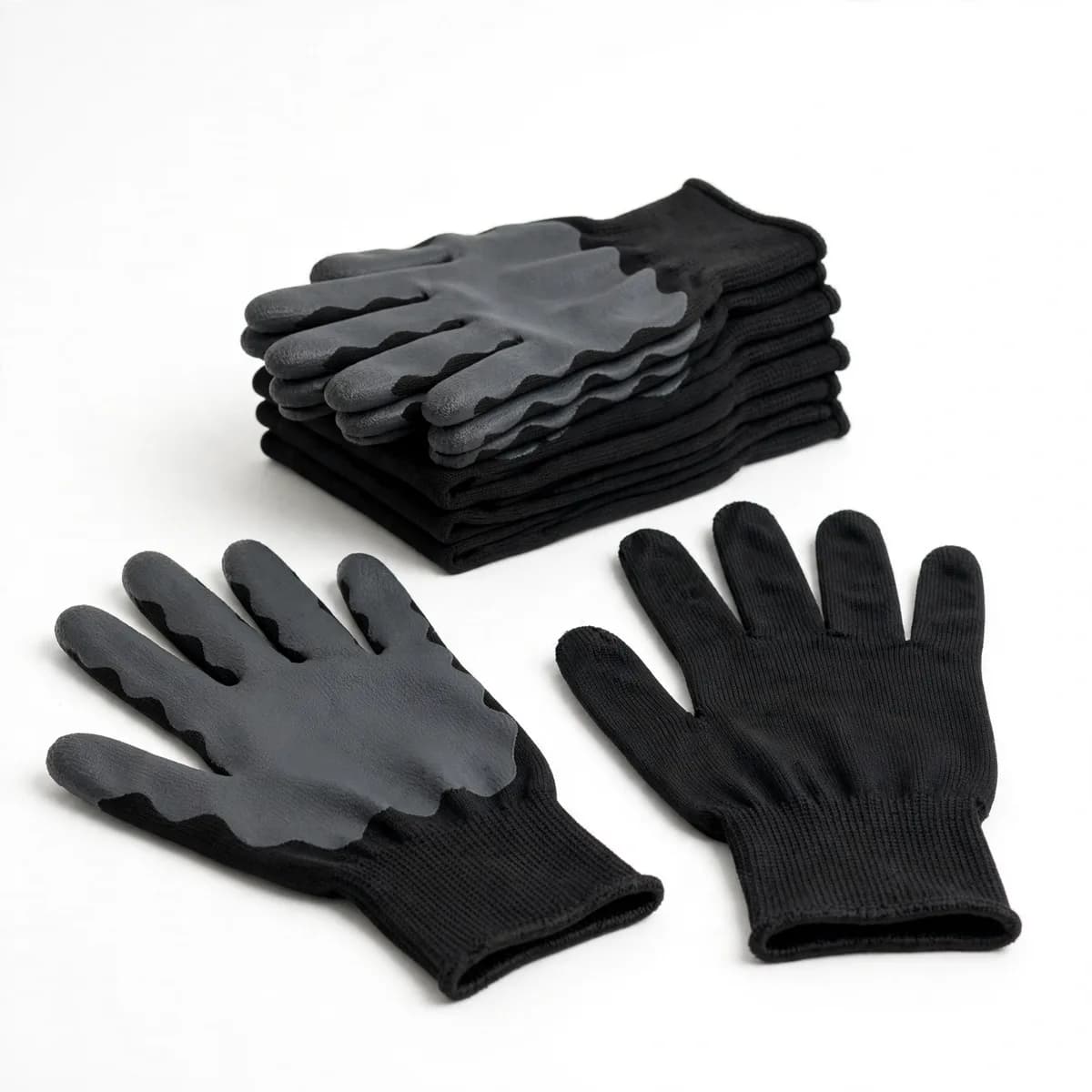 Deux gants sur fond blanc, paume enduite anthracite et dos en tricot noir, pile de paires pliées derrière
