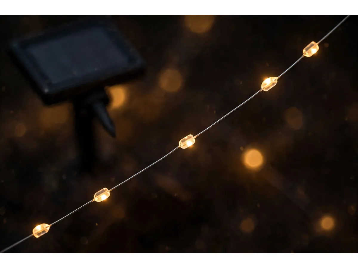 Macro de nuit sur le fil nu, les perles de diodes allumées en ambre chaud, le panneau flou en arrière-plan