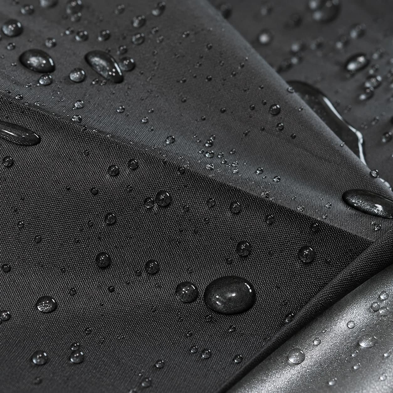 Gouttes de pluie perlant sur la toile noire, enduit argenté visible au pli