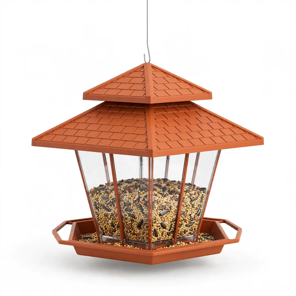 Mangeoire hexagonale suspendue, toit terracotta à relief de tuiles et silo transparent rempli de graines, sur fond blanc