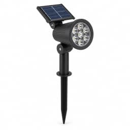Projecteur solaire noir sur fond blanc, tête cylindrique nervurée, panneau solaire incliné sur charnière et piquet à planter