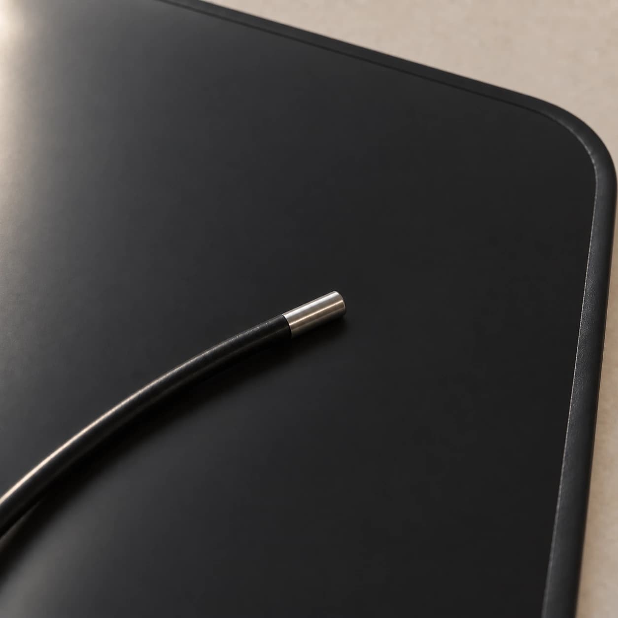 Extrémité métallique de la sonde posée sur la surface noire mate du tapis, près du bord thermosoudé