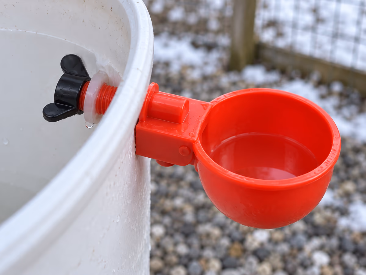 Pied d'un bol abreuvoir rouge vissé sur un bidon blanc, goutte d'eau au bord de la rondelle translucide après un dégel