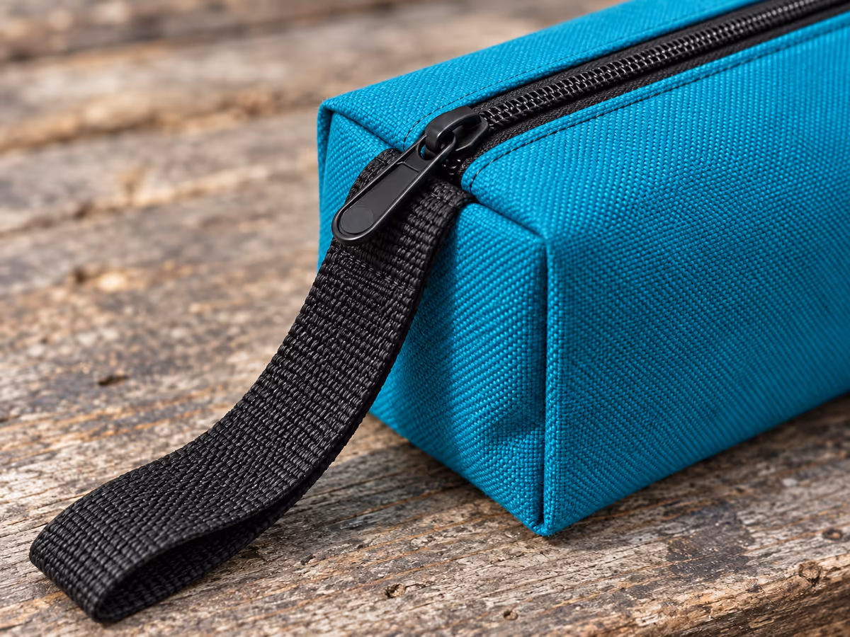 Gros plan du fond soufflet et de la sangle plate cousue à l'extrémité d'une pochette en toile turquoise