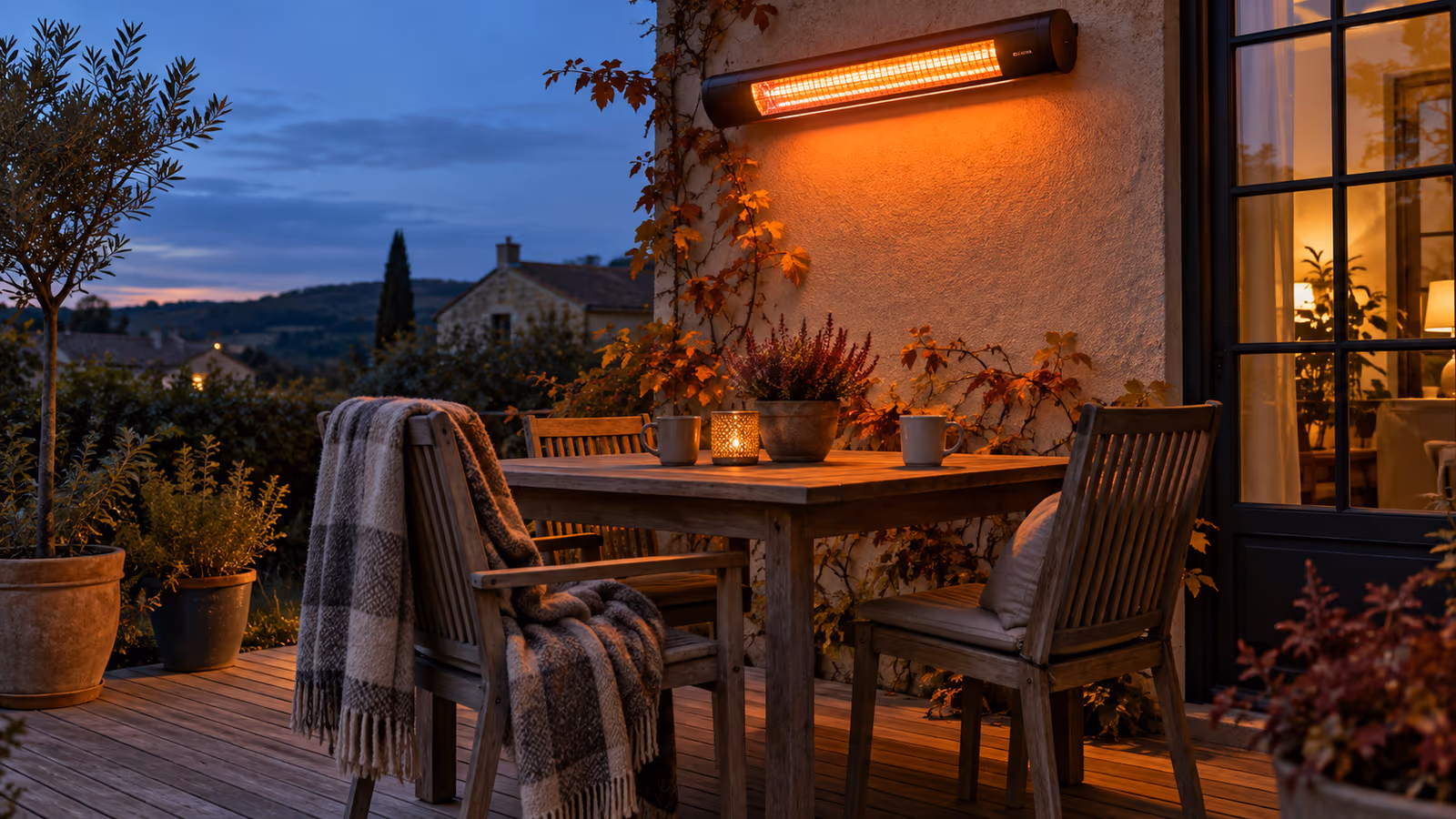 Terrasse en bois à la tombée du jour, un chauffage radiant à tube infrarouge fixé au mur diffuse une lueur orangée au-dessus d'une table et de chaises